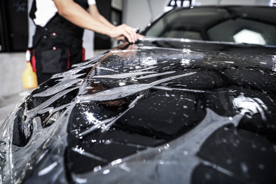 Clear protective film being precisely applied to the hood of a black vehicle at a Fort Worth window tinting and styling facility