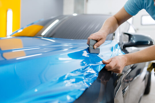 Expert installer using a squeegee tool to apply a vibrant blue gloss vinyl car wrap surface overlay